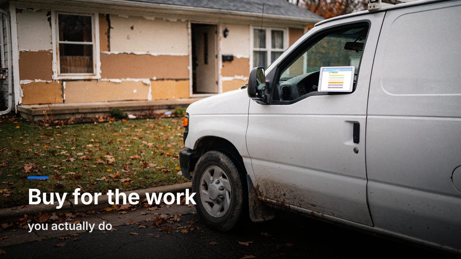 Unmarked restoration van at a curb by a flood-cut house, tablet with colored job rows on the dashboard, autumn leaves on the lawn.